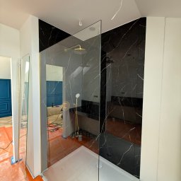 Anton Palianytsia ATOM - BUD - Nowoczesna kabina prysznicowa z czarnymi płytkami imitującymi marmur i złotą armaturą, w trakcie montażu, z widocznymi zabezpieczeniami podłogi.