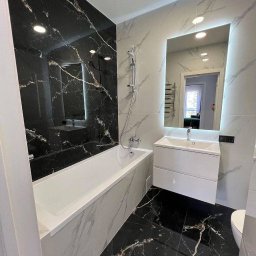 Anton Palianytsia ATOM - BUD - Elegancka łazienka z czarno-białymi płytkami imitującymi marmur, podświetlane lustro, biała wanna i umywalka. Nowoczesny design z akcentem luksusu.