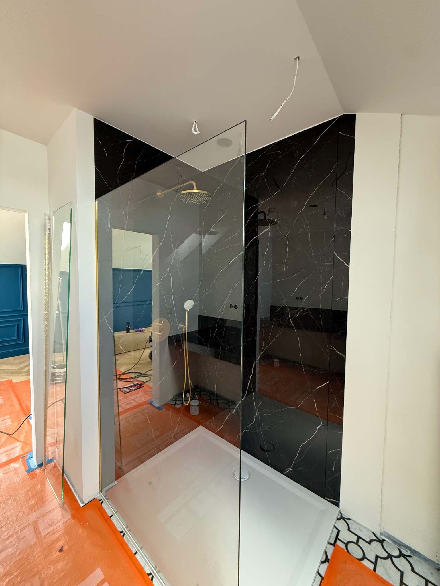 Nowoczesna kabina prysznicowa z czarnymi płytkami imitującymi marmur i złotą armaturą, w trakcie montażu, z widocznymi zabezpieczeniami podłogi.