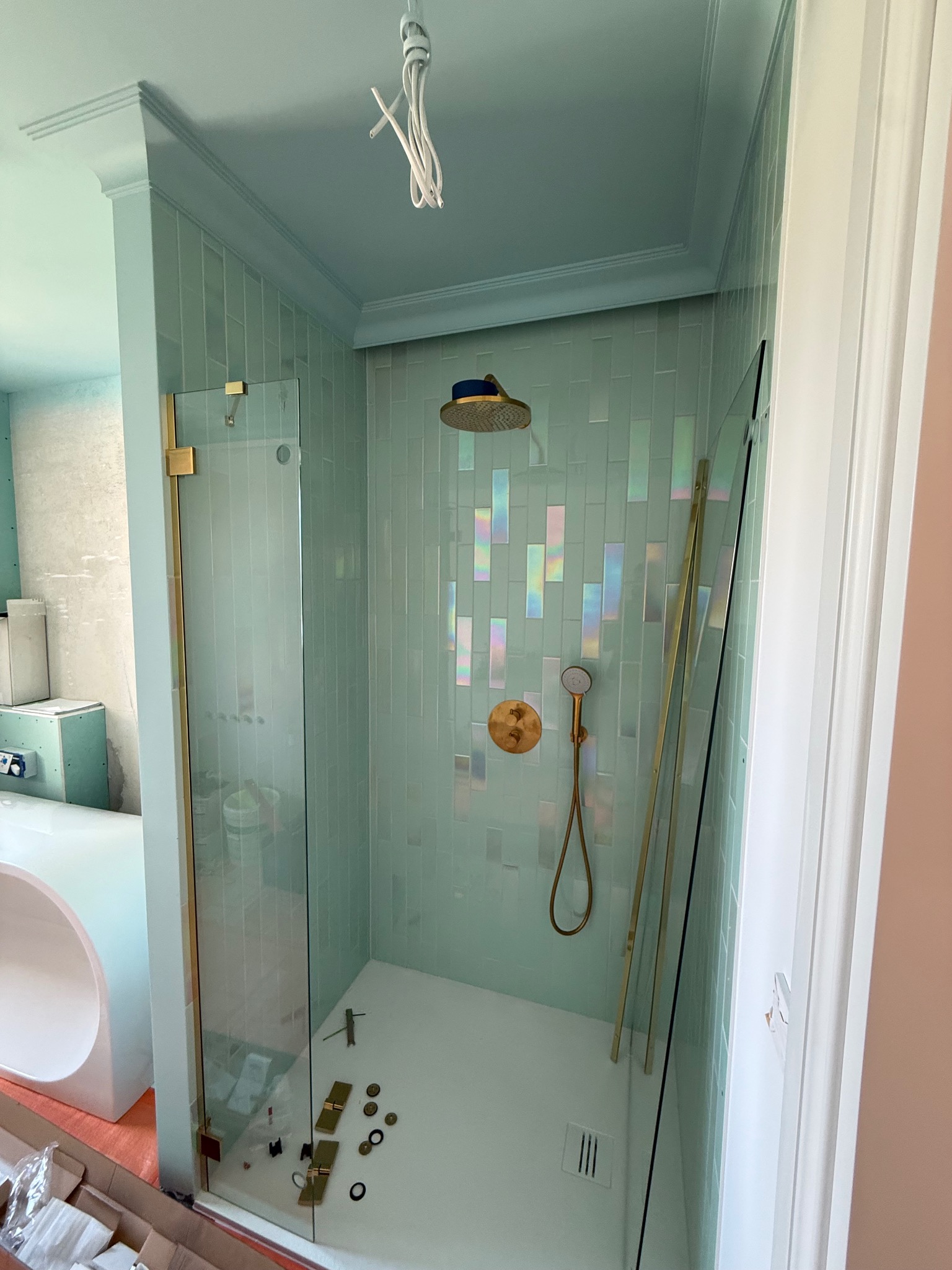 Nowoczesna kabina prysznicowa z turkusowymi płytkami i złotymi elementami wykończeniowymi. Widoczne narzędzia i akcesoria montażowe.