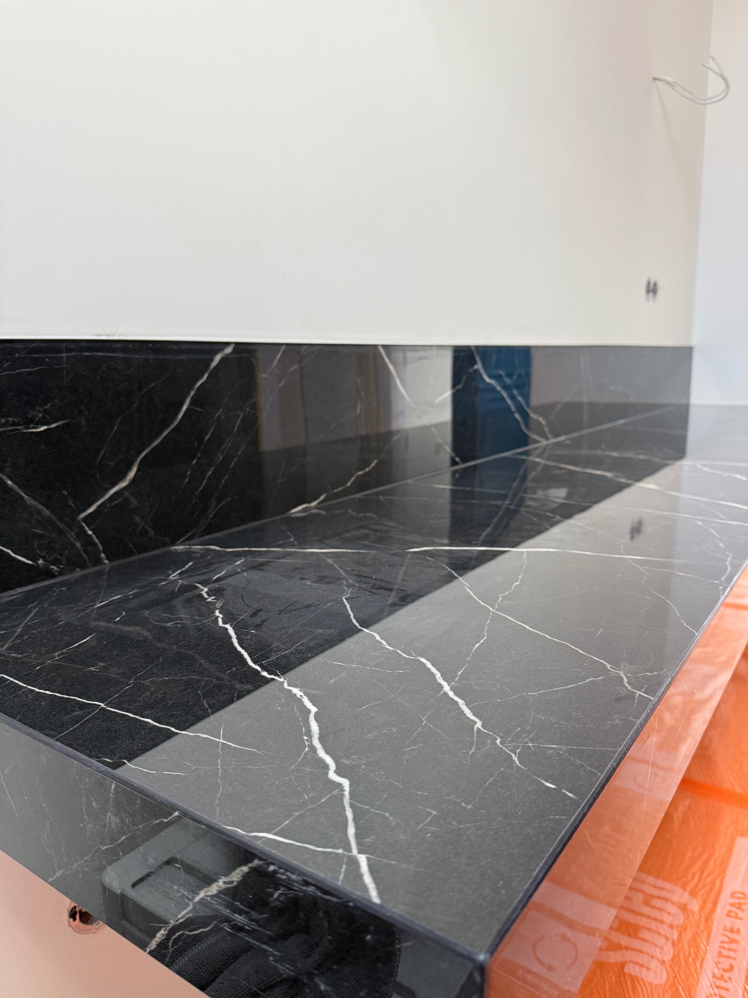 Czarny blat z marmurowym wzorem, prawdopodobnie w łazience lub kuchni, z widocznymi przewodami elektrycznymi wystającymi ze ściany.