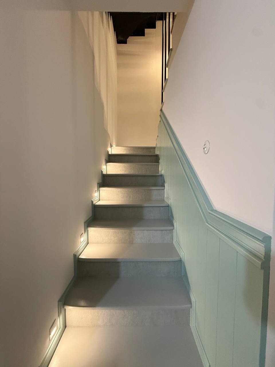 Odnowione schody wewnętrzne z szarymi stopniami i panelami ściennymi w odcieniach błękitu. Oświetlenie punktowe przy stopniach. Widok z dołu.