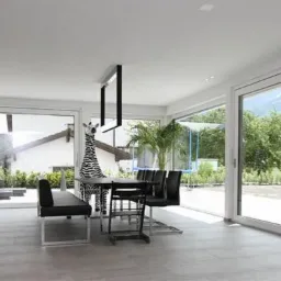 Jasne wnętrze z dużymi przesuwnymi oknami wychodzącymi na zielony ogród i góry w tle, minimalistyczna kuchnia po lewej, stół jadalny z czarnymi krzesłami i dekoracyjną figurą zebry.