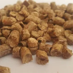 Kupka brązowych, cylindrycznych peletek z widoczną strukturą włókien drzewnych na białym tle.