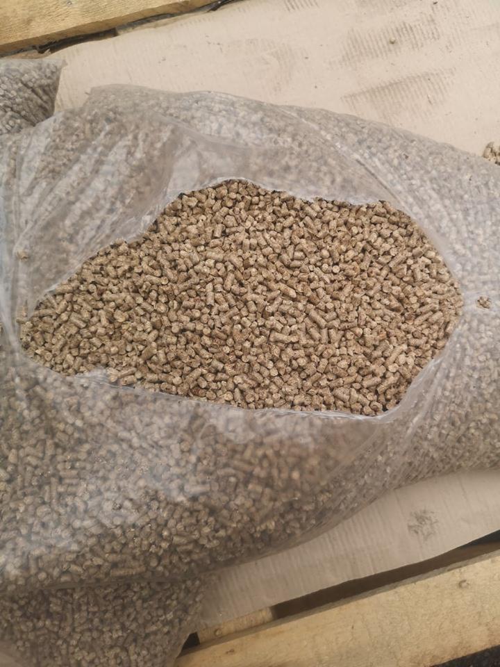 Worek z przezroczystego tworzywa wypełniony jasnobrązowym granulatem na drewnianej palecie. Część granulatu rozsypana obok worka.