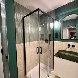 Mebel-Ol - Nowoczesna łazienka z kabiną prysznicową typu walk-in z czarnymi profilami, zieloną umywalką i ścianami w odcieniach zieleni i beżu. Widoczne oświetlenie i lustro.