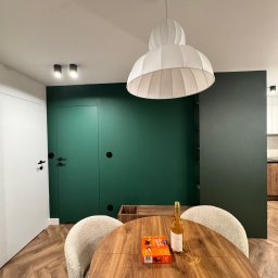 Mebel-Ol - Nowoczesna jadalnia: okrągły drewniany stół z krzesłami boucle, designerska lampa, zielona ściana z ukrytymi drzwiami i parkiet w jodełkę. Minimalistyczny wystrój.