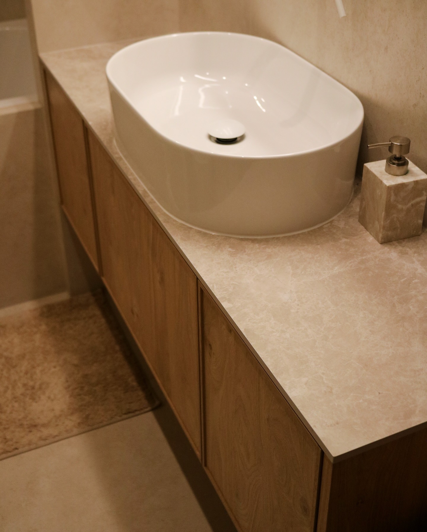 Nowoczesna łazienka: owalna umywalka nablatowa na drewnianej szafce z marmurowym blatem, obok dozownik mydła z tego samego marmuru. Ujęcie z bliska.