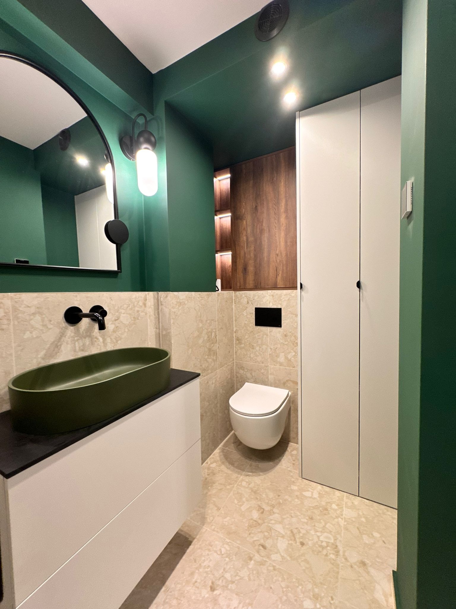 Nowoczesna łazienka w odcieniach zieleni i beżu: owalna umywalka, minimalistyczna toaleta, szafka z szufladami i lustro z oświetleniem. Eleganckie wykończenie.