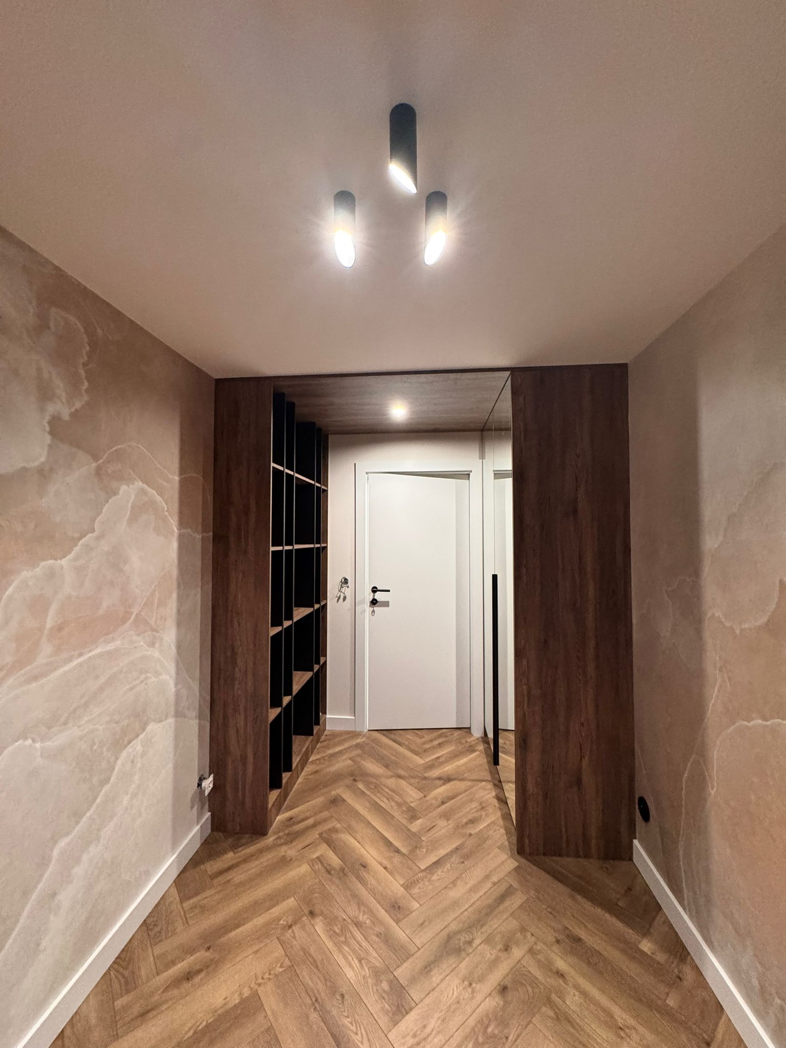 Nowoczesny przedpokój z drewnianą podłogą w jodełkę, marmurkowymi ścianami i zabudową szafy z lustrem. Minimalistyczne oświetlenie sufitowe.