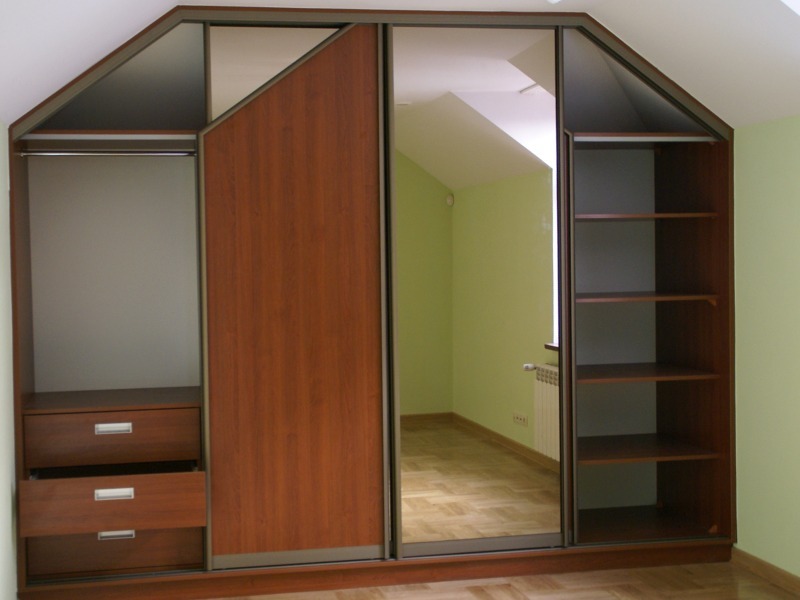 Szafa wnękowa z przesuwnymi drzwiami i lustrem, dopasowana do skosu poddasza, z drewnianymi elementami i półkami.