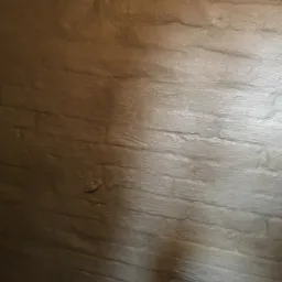 Szara, szorstka powierzchnia imitująca mur z kamieni, prawdopodobnie pokryta hydroizolacją bitumiczną, widoczna pod światło.