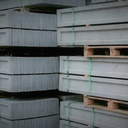 Szare betonowe prefabrykaty na drewnianych paletach, zabezpieczone zielonymi taśmami.