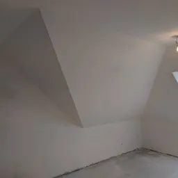 Poddasze przed wykończeniem: surowe ściany i podłoga, widoczne okno dachowe i pojedyncza żarówka