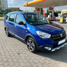 Niebieski samoch&oacute;d typu kombi na tle stacji benzynowej Shell, widok z boku na kostce brukowej.