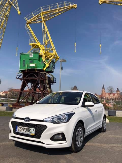 Biały samochód osobowy Hyundai zaparkowany na tle portowych dźwigów i zabudowy miejskiej.