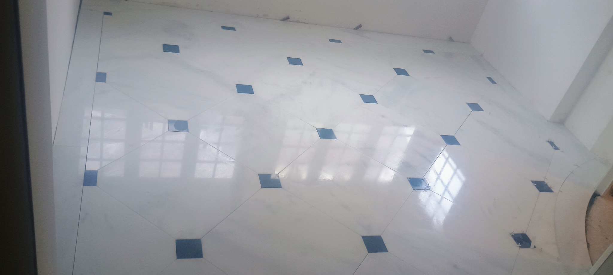 Biała podłoga z jasnych płytek z ciemnoniebieskimi kwadratami w rogach płytek, odbicie okna na powierzchni