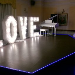 Mirosław Ciurej - Scena z napisem LOVE wykonanym z podświetlanych liter obitych futerkiem, białe pianino w tle, niebieskie oświetlenie krawędzi sceny, sala bankietowa.
