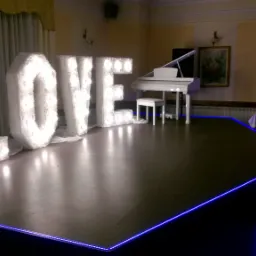 Scena z napisem LOVE wykonanym z podświetlanych liter obitych futerkiem, białe pianino w tle, niebieskie oświetlenie krawędzi sceny, sala bankietowa.