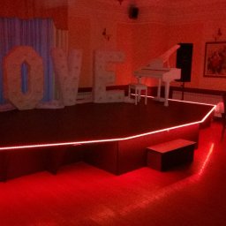 Mirosław Ciurej - Scena z napisem LOVE podświetlonym na czerwono, białe pianino i stół w tle w czerwonym oświetleniu.