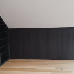 Mirosław Ciurej - Ciemna zabudowa meblowa na wymiar w pokoju na poddaszu, z otwartym regałem na ścianie szczytowej i szafą przesuwną z podświetleniem LED.