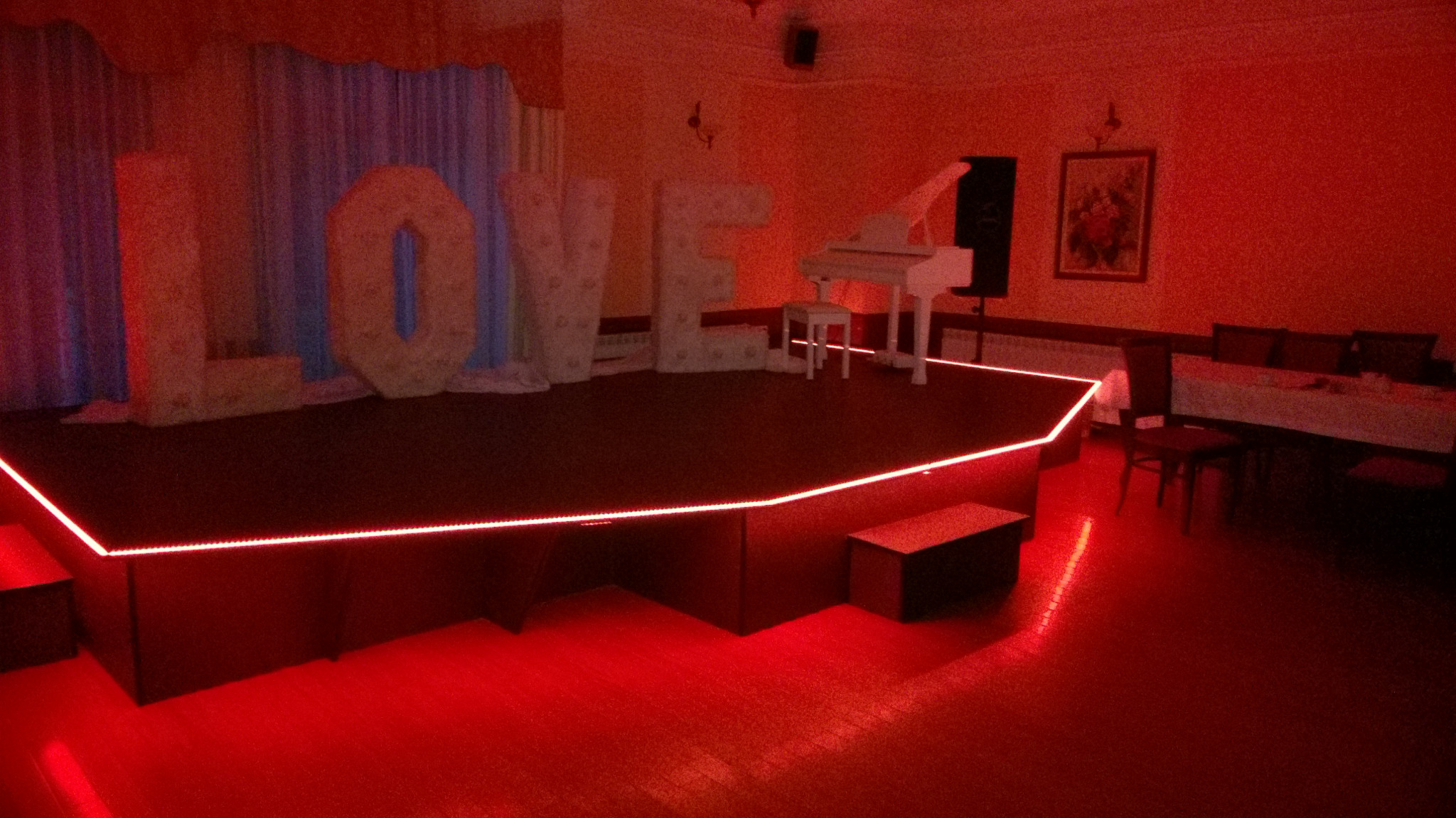 Scena z napisem LOVE podświetlonym na czerwono, białe pianino i stół w tle w czerwonym oświetleniu.