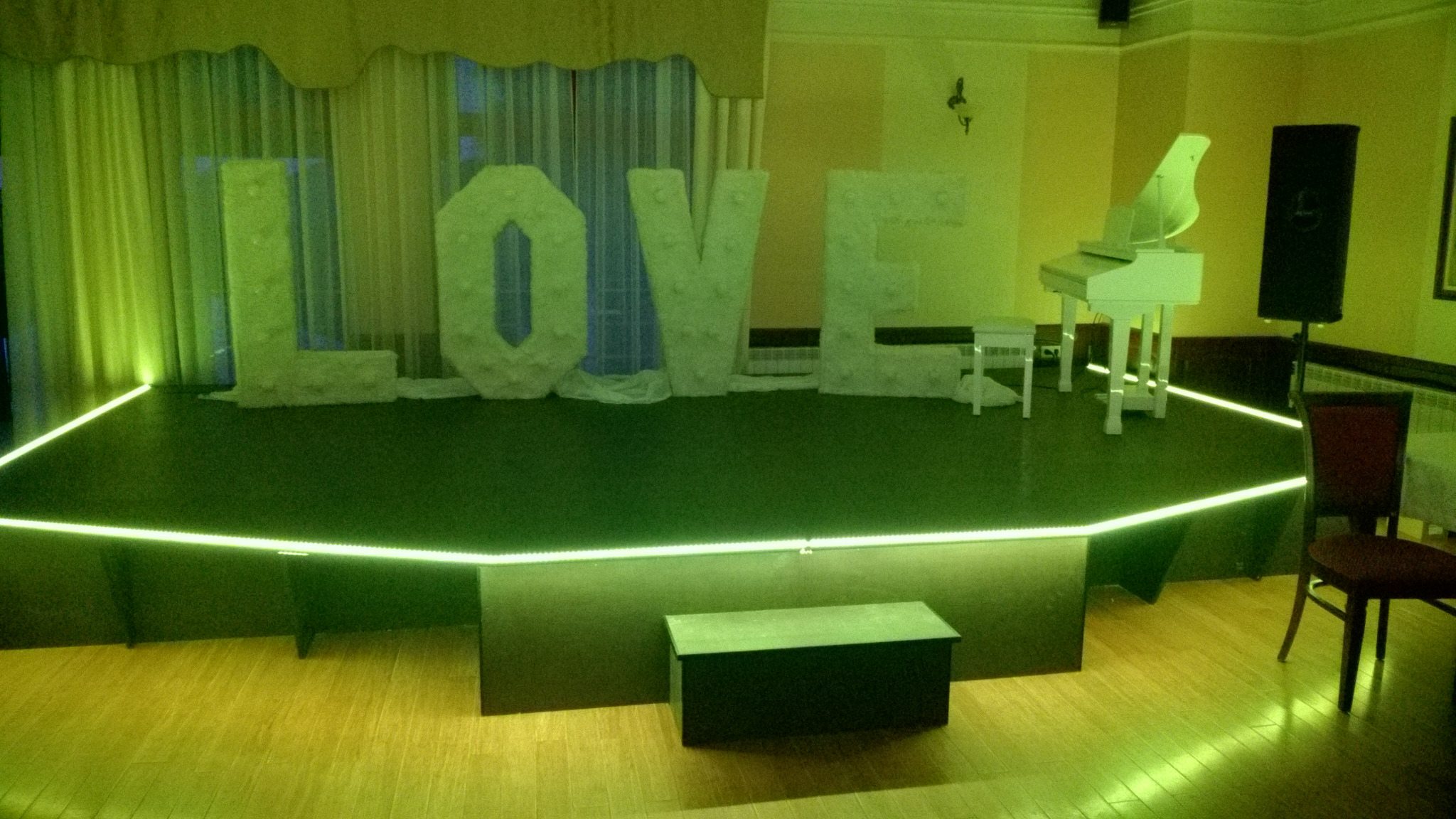 Scena z napisem LOVE z dekoracyjnych liter, podświetlona zielonymi światłami, białe pianino na podeście, przygotowana na imprezę.