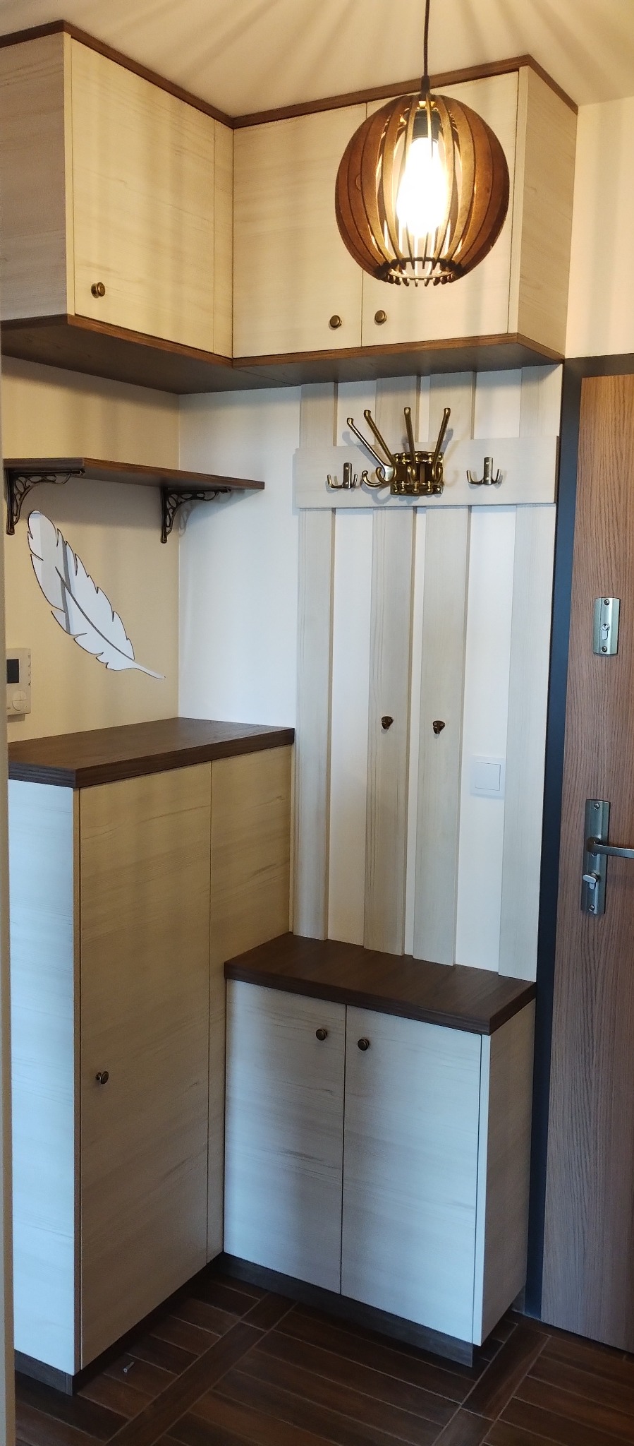 Korytarz z zabudową meblową: szafka na buty z siedziskiem, szafa, półki z dekoracyjnymi wspornikami, panel z wieszakami i ażurowa lampa sufitowa.