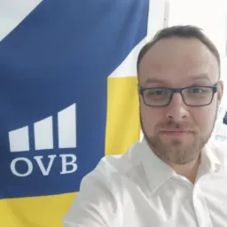 Portret mężczyzny w okularach i białej koszuli na tle flagi OVB we Wrocławiu.