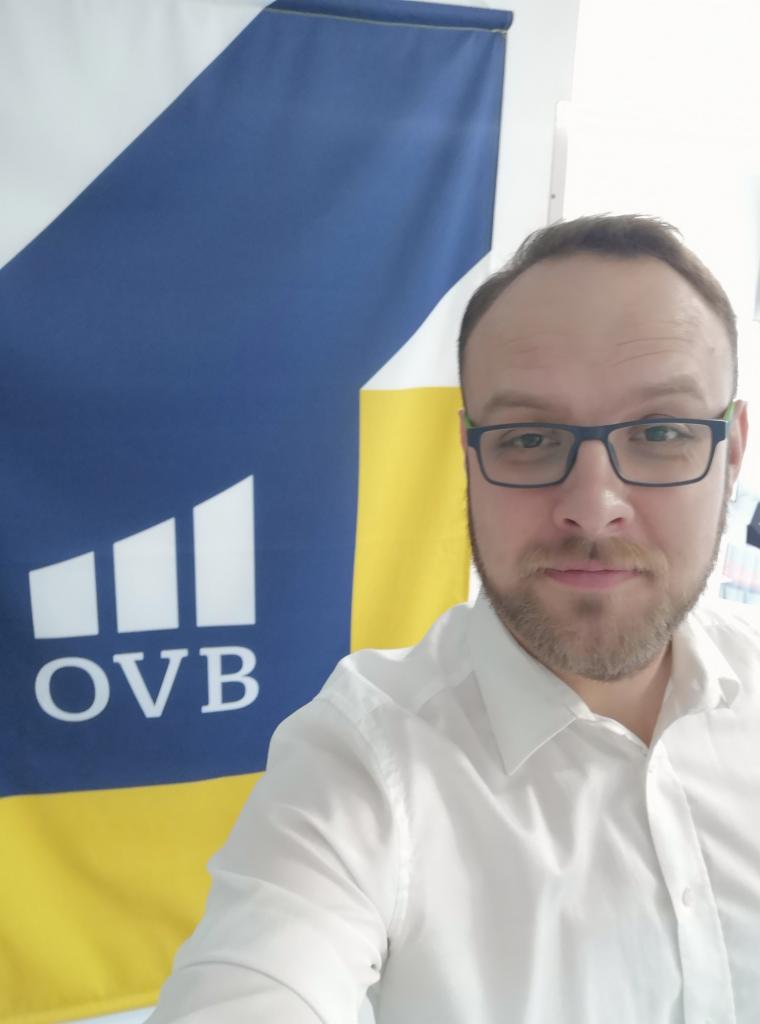 Portret mężczyzny w okularach i białej koszuli na tle flagi OVB we Wrocławiu.