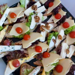 Czarny talerz z kanapkami z różnymi serami, pomidorkami cherry, orzechami włoskimi i sałatą na kromkach pieczywa.