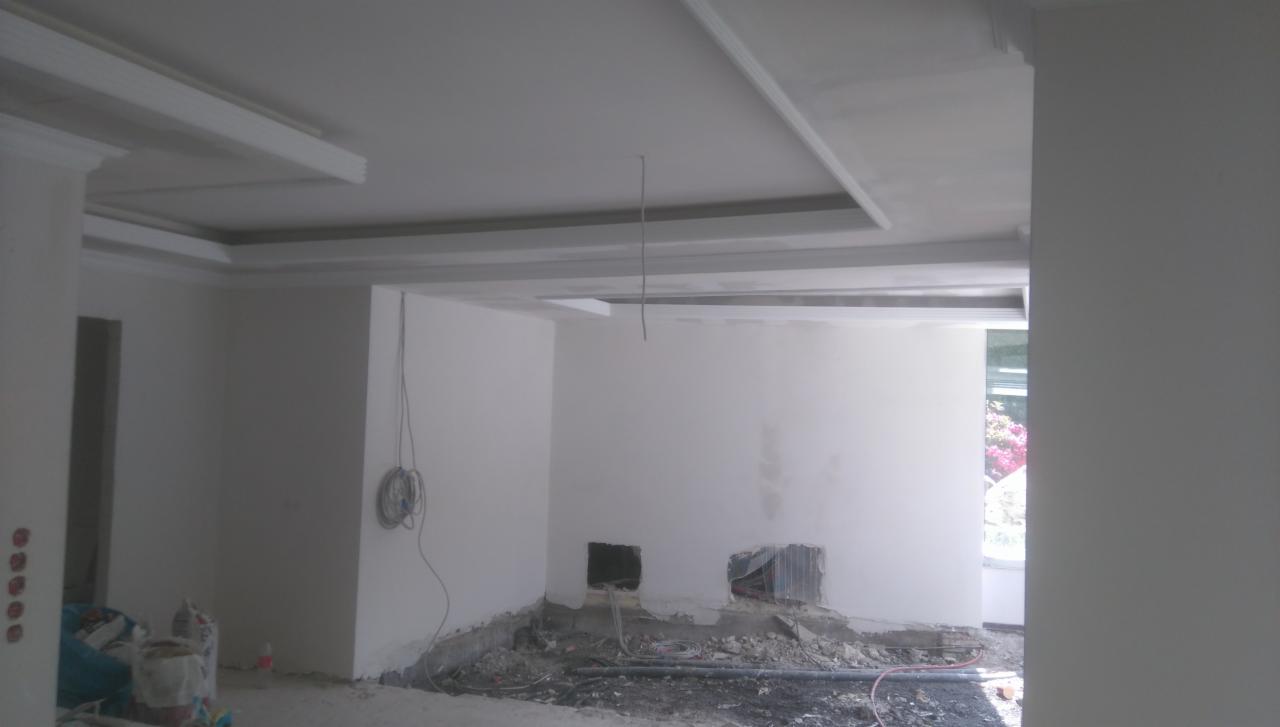 Wnętrze w trakcie prac wykończeniowych: sufit z dekoracyjnymi listwami, ściany po gładziowaniu, widoczne instalacje elektryczne i gruz na podłodze.