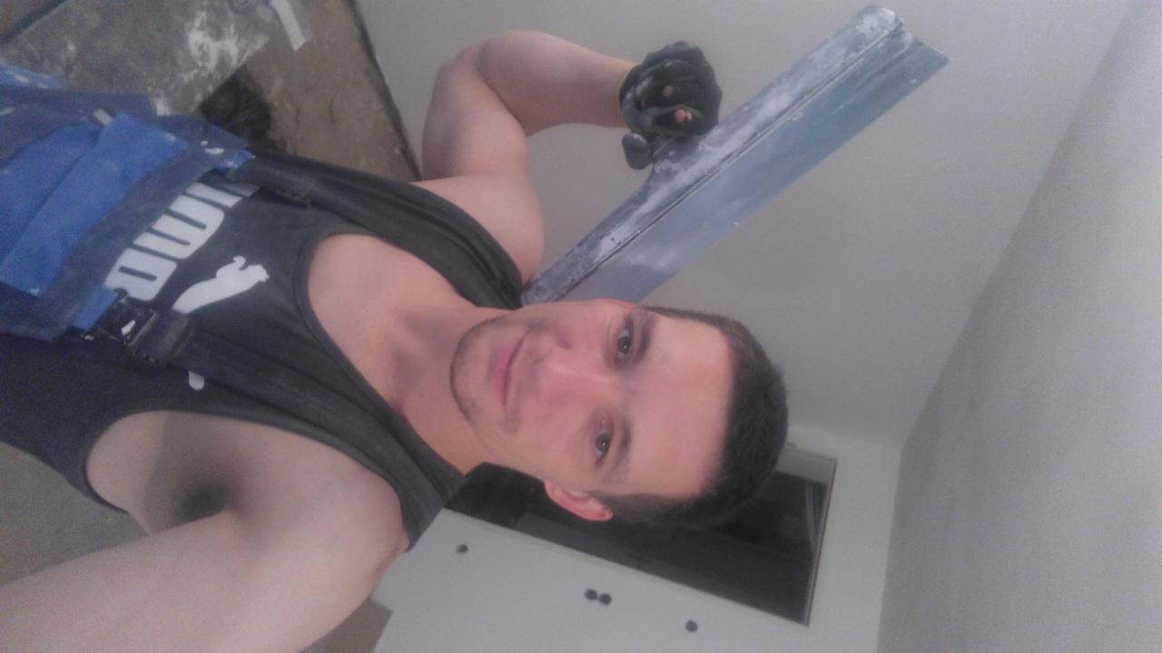 Mężczyzna z gładzią na szpachli, w pomieszczeniu po gładziowaniu. Widoczne ślady gładzi na ścianach i suficie. Selfie w trakcie pracy.