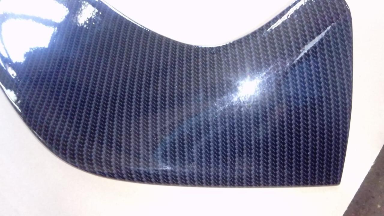 Fragment formy z ciemnego włókna węglowego z widocznymi refleksami światła i delikatną krzywizną.