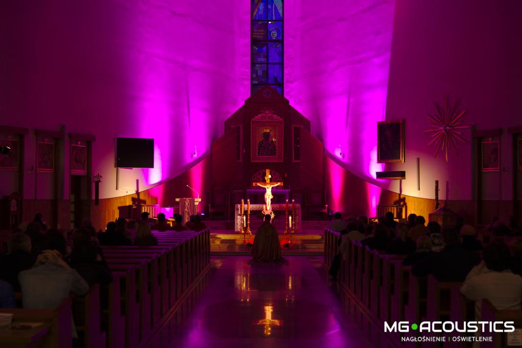 Kościół oświetlony fioletowym światłem, widoczny ołtarz i wierni siedzący w ławkach, na podłodze odbicie światła, w prawym dolnym rogu logo firmy MG Acoustics.