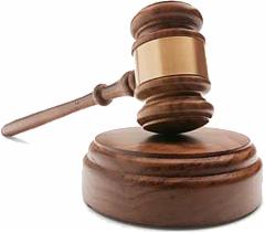 Drewniany młotek sędziowski na okrągłej podstawie, z widocznym złoconym elementem na głowicy, oświetlony z góry, rzucający cień na białe tło.