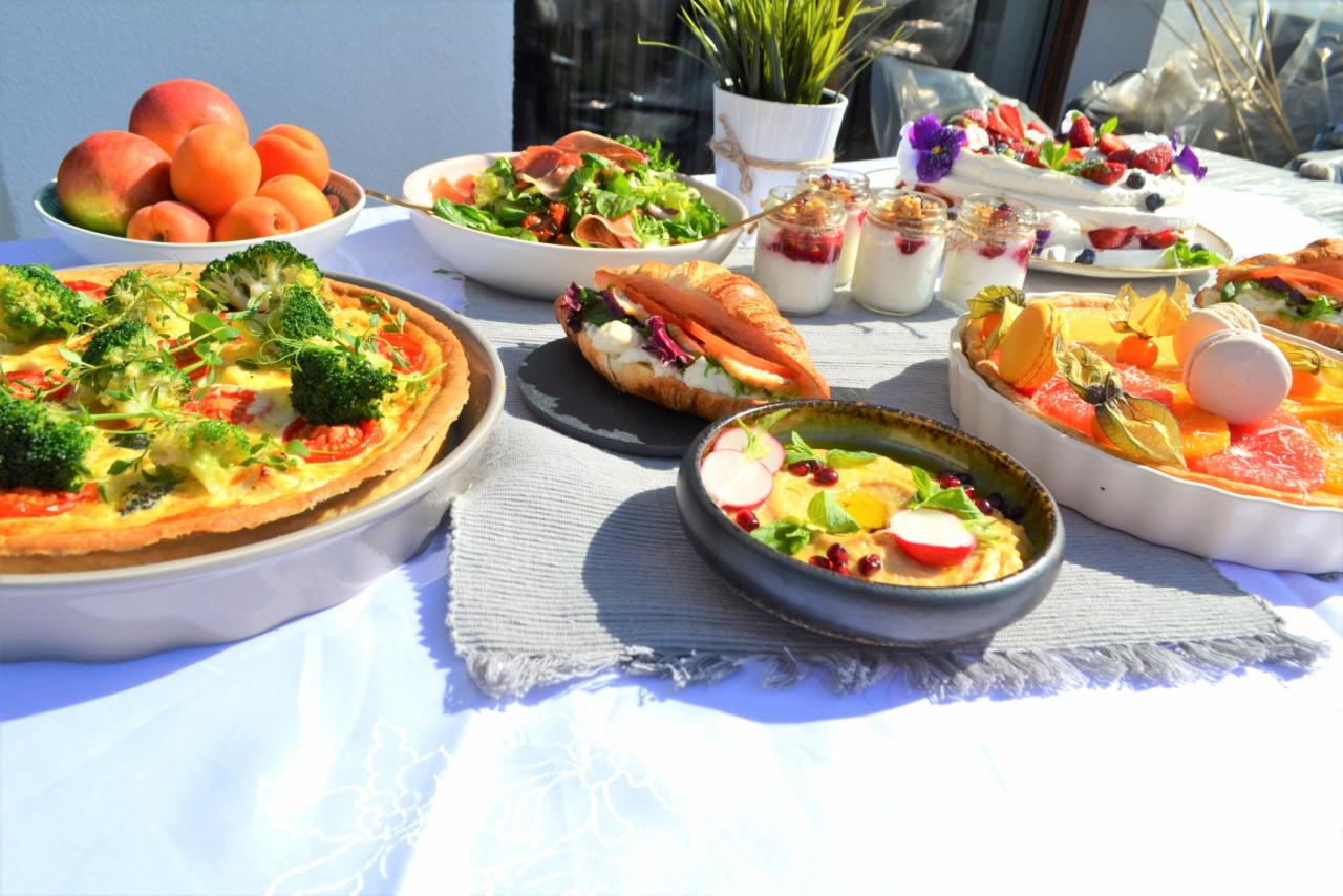 Bogato zastawiony stół we Wrocławiu z różnorodnymi daniami: quiche z brokułami, sałatka z szynką parmeńską, croissant z nadzieniem, kremowe desery w słoiczkach i tarta owocowa z physalis...