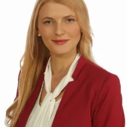 Portret uśmiechniętej blondynki w czerwonej marynarce na białym tle.