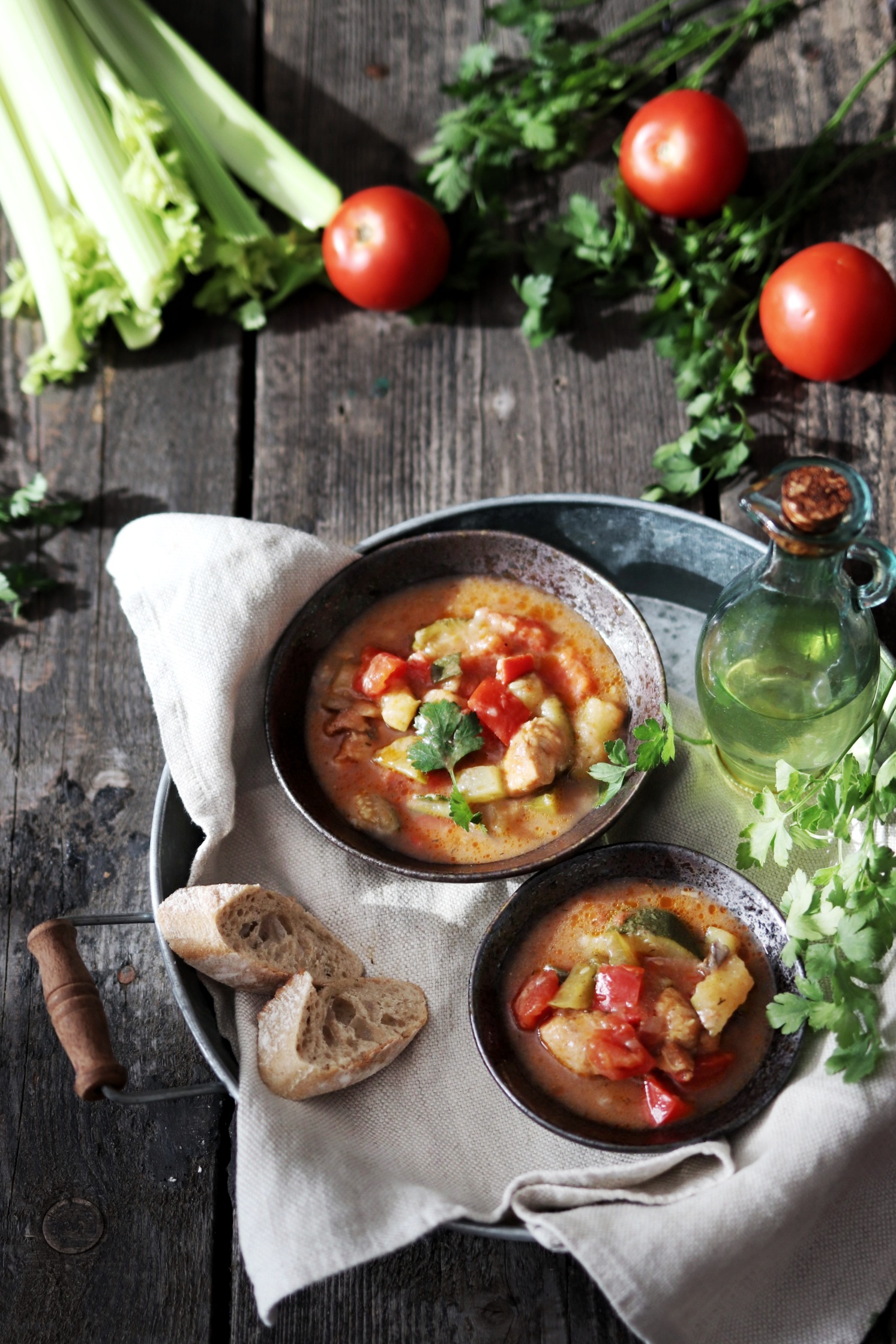 Dwie miski z dietetyczną zupą warzywną na metalowej tacy, obok chleb, oliwa i świeże warzywa, aranżacja cateringu dietetycznego z Sędziszowa Małopolskiego na rustykalnym drewnianym stole.