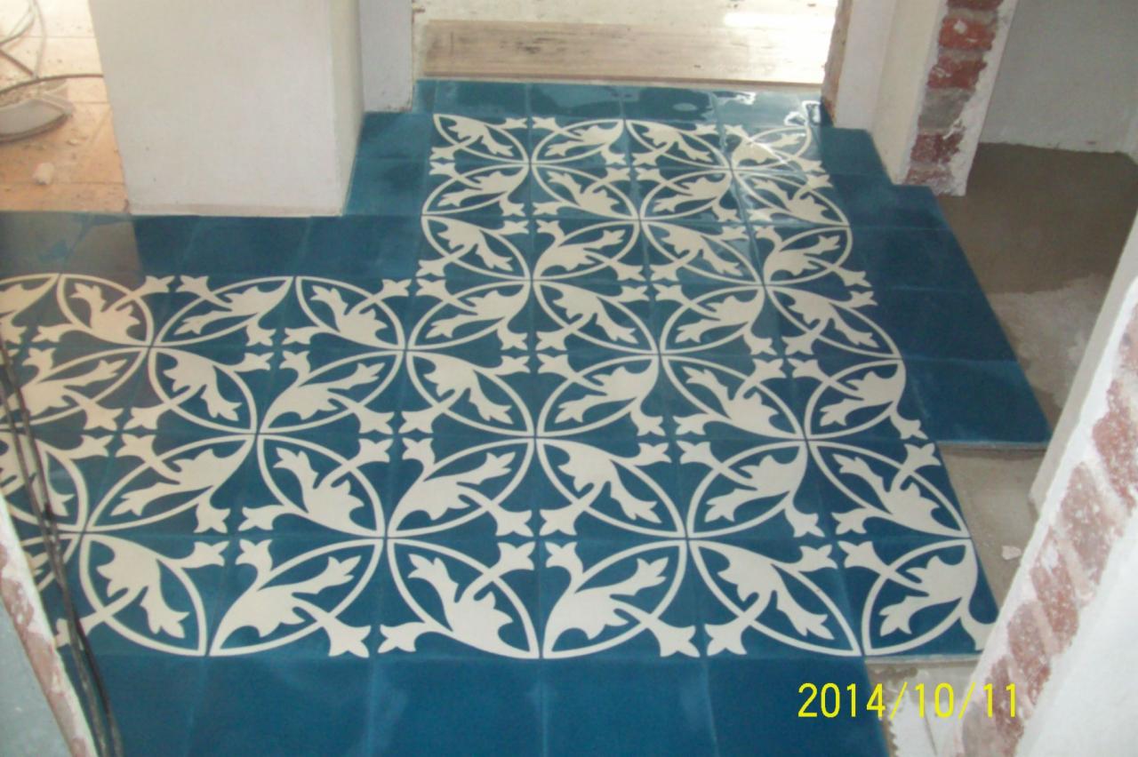 Niebieskie płytki podłogowe z kremowobiałym, roślinnym wzorem, ułożone w przejściu między pomieszczeniami; widoczne surowe ściany i data wykonania zdjęcia.