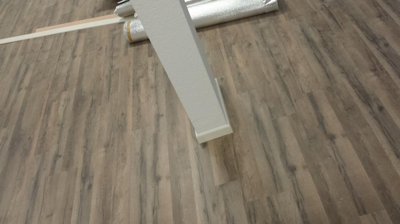 Ułożona podłoga z paneli imitujących drewno, widoczna biała listwa przypodłogowa i folia izolacyjna w rolce.