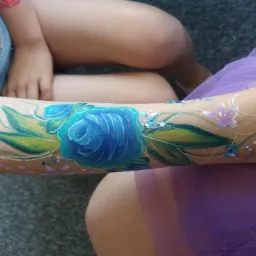 Ręka dziecka z namalowaną niebieską różą i brokatem, otoczona drobnymi kwiatkami i białymi ornamentami.