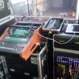 Profesjonalny mikser dźwięku Allen & Heath SQ-5 z drewnianymi panelami bocznymi, umieszczony na skrzyni transportowej, obok skrzynie z logiem firmy, kable i tablet na drugim urządzeniu. Sprzęt...