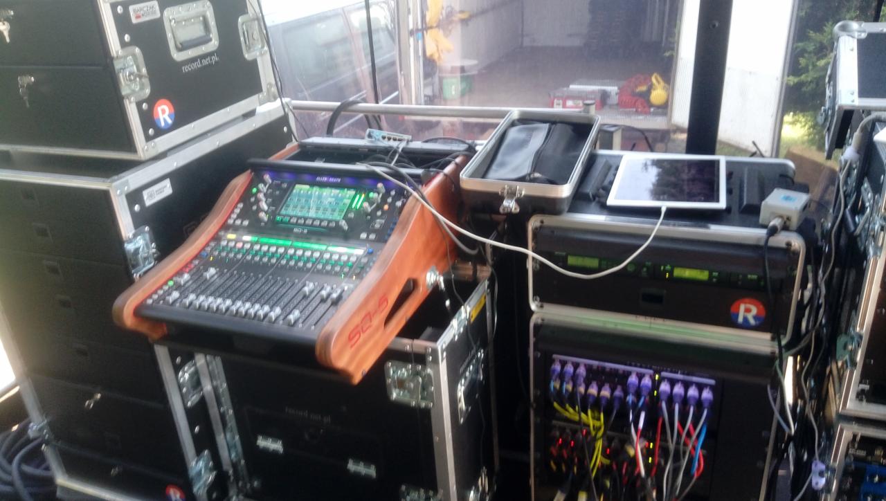 Profesjonalny mikser dźwięku Allen & Heath SQ-5 z drewnianymi panelami bocznymi, umieszczony na skrzyni transportowej, obok skrzynie z logiem firmy, kable i tablet na drugim urządzeniu. Sprzęt...