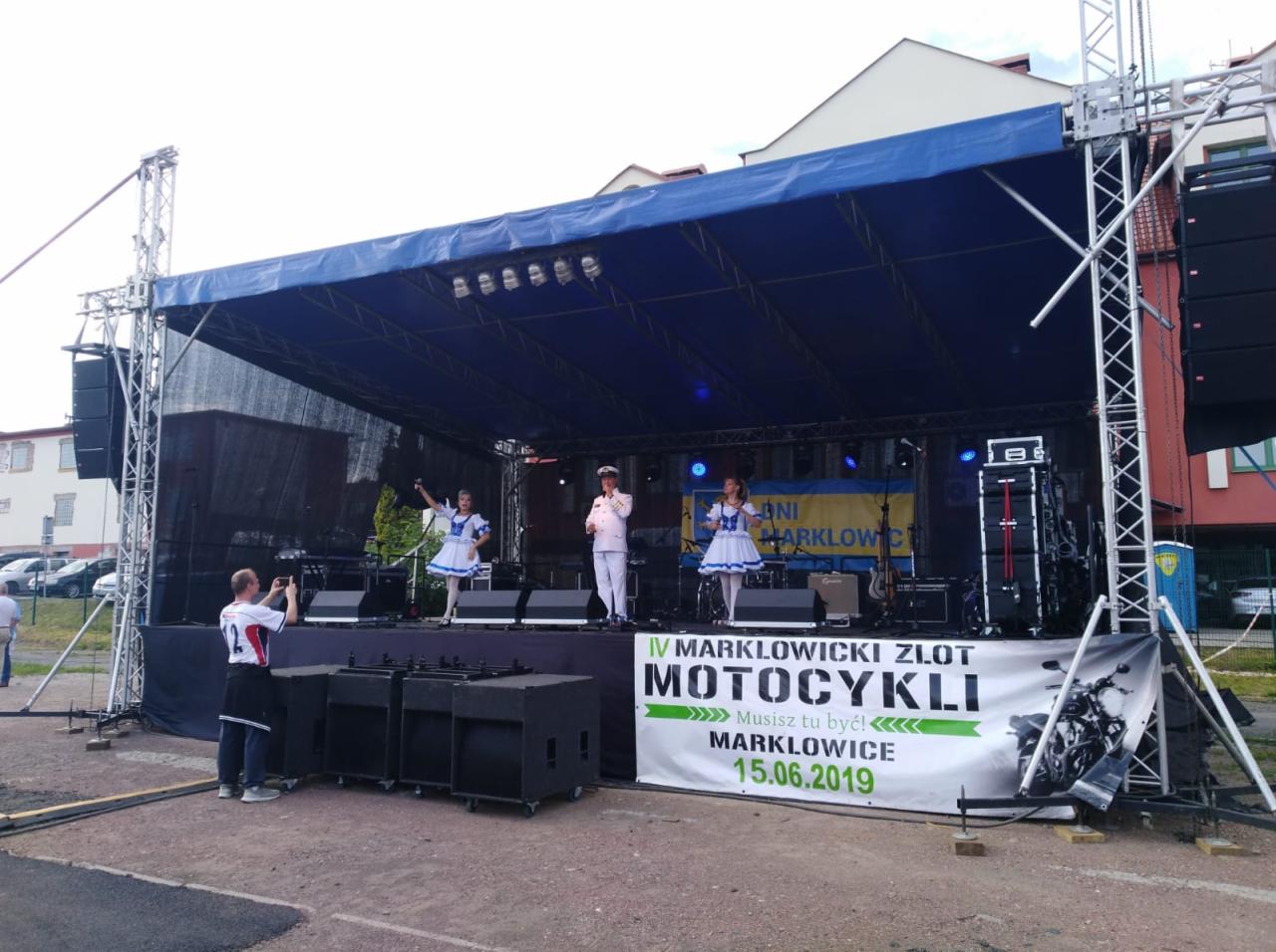 Scena plenerowa z występem artystycznym podczas IV Marklowickiego Zlotu Motocykli, z trzema osobami na scenie w strojach marynarskich, widoczny baner reklamowy z datą 15.06.2019, nagłośnienie...