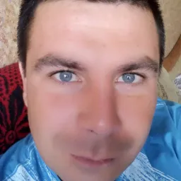 Portret mężczyzny z bliska, widoczne niebieskie oczy i wzorzysta niebieska koszulka.