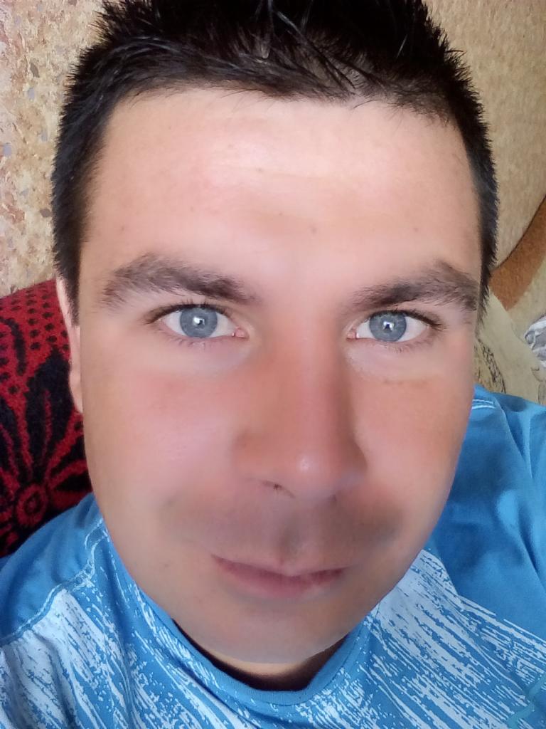 Portret mężczyzny z bliska, widoczne niebieskie oczy i wzorzysta niebieska koszulka.