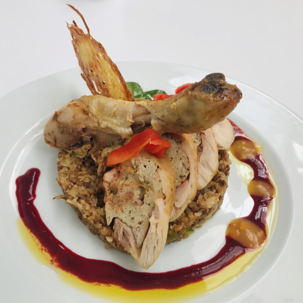 Elegancko podane danie: pieczony kurczak z farszem, ułożony na kaszy gryczanej, udekorowany sosem owocowym, chipsem i papryką na białym talerzu.