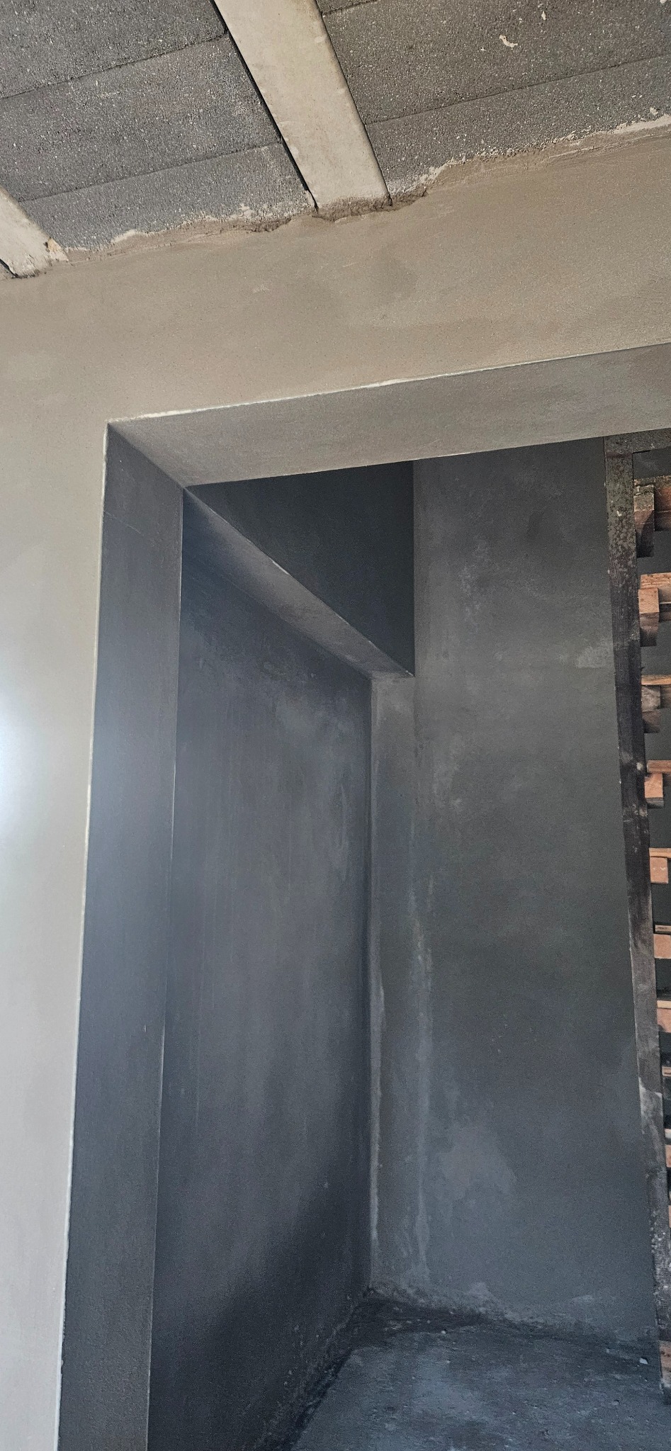 Surowe wnętrze w trakcie prac wykończeniowych: świeżo nałożony tynk maszynowy na ścianach i suficie, widoczne bloczki betonowe na suficie, surowy stan wykończenia wnęki drzwiowej.