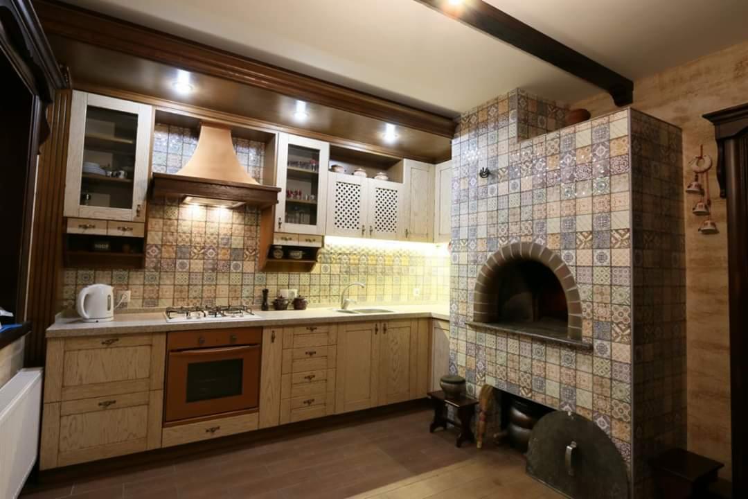 Rustykalna kuchnia z drewnianymi szafkami, ceramiczną mozaiką na ścianach i piecem chlebowym wykończonym w stylu patchworkowym z płytek.